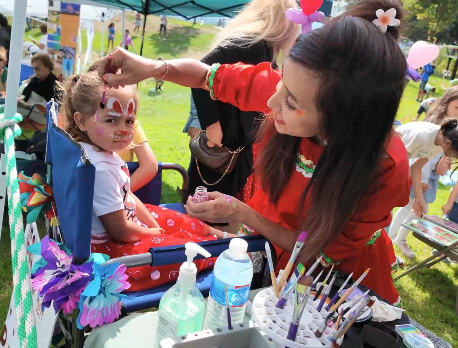Face painting a colorful design on a girl at an outdoor park birthday party