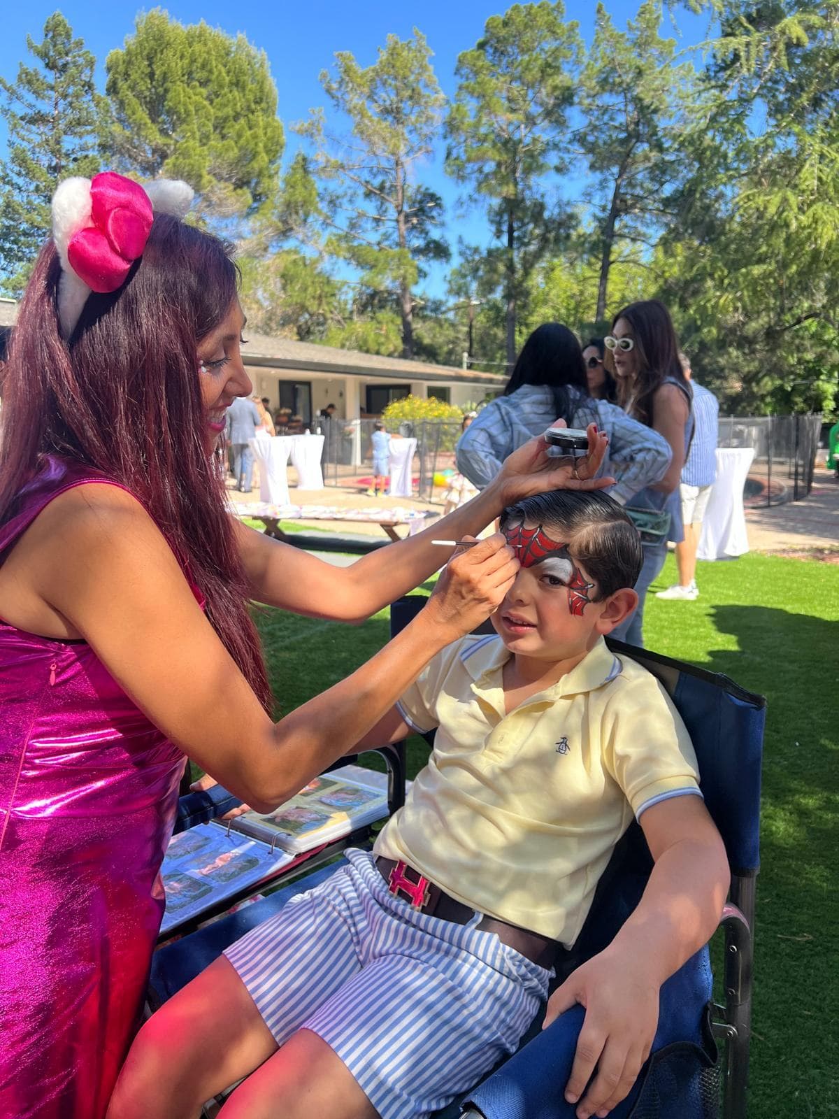 Face painter painting a superhero design on a boy at an outdoor birthday party
